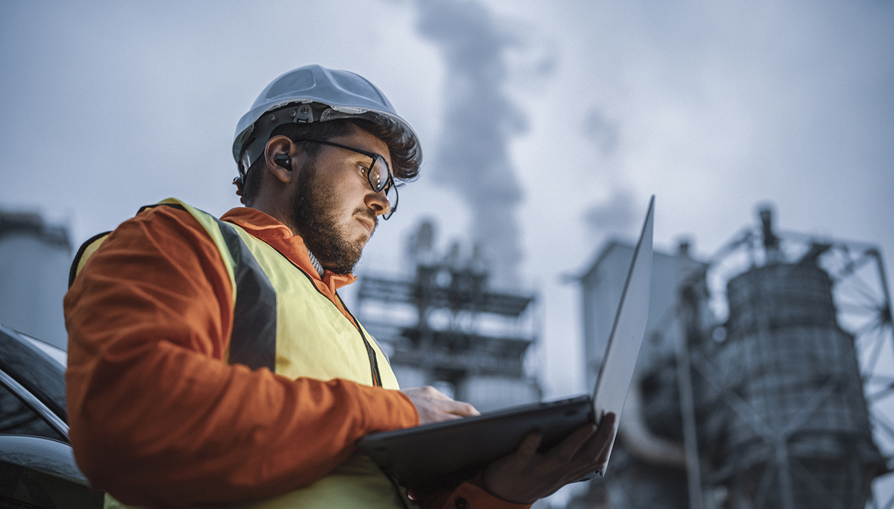 A shot of an young engineer wearing a helmet and using a laptop and hands free device during his night shirt in the oil rafinery. Engineering concept.